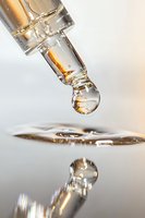 Crystal clear water drop falling and reflecting in mirror surface, captured in macro with golden light highlights showing liquid surface tension and refraction.