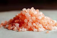 Pink Himalayan salt crystals in pile on white surface, macro close up view showing mineral texture and natural pink hues in soft lighting.