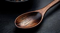 Rustic wooden spoon with rich brown grain texture on dark background, dramatic lighting highlights natural wood patterns, culinary and kitchen decor concept.