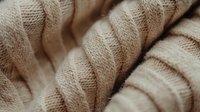 Soft beige knitted fabric with twisted rope pattern macro shot showing detailed texture of warm wool sweater material in neutral tones.
