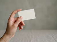 Hand holding blank white business card against neutral gray background for branding and corporate identity mockup purposes.
