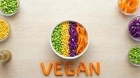 Colorful vegan bowl with edamame, corn, red cabbage and carrots, VEGAN lettering made of carrots on wooden background, top view.