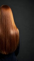 Rear view of woman with long straight shiny copper red hair against dark background. Professional hair care and salon treatment concept.