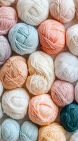 Soft pastel yarn balls in peach, mint, and cream colors arranged in flat lay composition, showing gentle texture of wool threads for knitting and crafting projects.