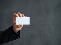 Male professional holding blank white business card against gray textured background. Suitable for corporate branding, business identity, networking, and marketing materials.