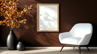 Modern minimalist interior with white armchair, empty wooden frame and black vase with golden leaves against dark brown wall, sunlight casting natural shadows.