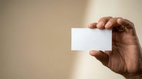 Hand of a man with dark skin tone holding a blank white business card or paper against a neutral beige background, suitable for corporate branding and professional mockups.