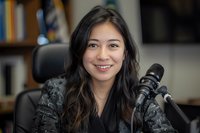 Young Asian woman podcaster smiling at camera while recording content in home studio setup with professional microphone and recording equipment.