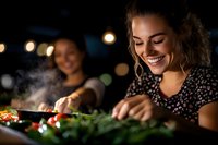 Young Hispanic woman smiling while cooking fresh vegetables on outdoor grill at night. Bokeh lights and steam create warm atmosphere for summer entertaining.