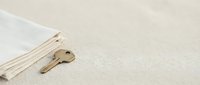Brass key resting on folded linen fabric against neutral textured background, symbolizing security, access, and home ownership for design projects.