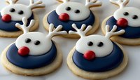 Festive reindeer sugar cookies decorated with royal icing featuring white antlers, black eyes, and red nose on navy blue base. Holiday baking and party treats.
