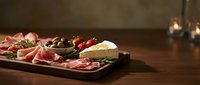 Gourmet charcuterie board with assorted meats, cheese, olives and strawberries on wooden table. Appetizer platter for entertaining and wine pairing occasions.