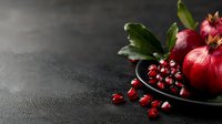 Ripe pomegranate with scattered seeds and fresh green leaves on dark slate surface, ideal for food styling, culinary content, and healthy eating promotions.