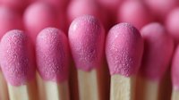 Pink matchsticks arranged in neat rows showing textured match heads in macro photography, creating repetitive pattern with soft focus and shallow depth of field.