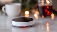 Smart home speaker device on table with ambient lighting, glowing LED indicators and blurred coffee cup in background creating cozy atmosphere for home automation.