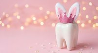 Tooth fairy concept with white molar wearing pink glittery crown and bunny ears on soft pink background with warm bokeh lights for dental care campaigns.