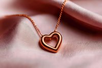 Rose gold heart pendant necklace on soft pink silk fabric background with gentle folds creating romantic mood and luxury jewelry presentation.