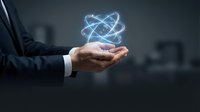 Businessman holding glowing atomic structure hologram in cupped hands representing science, technology innovation and nuclear energy concepts in modern office.