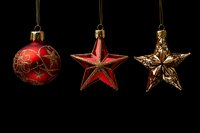 Red and gold Christmas ornaments hanging against black background - round bauble and two stars with vintage metallic finish and decorative patterns.