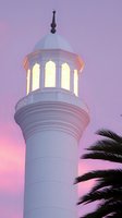 White mosque minaret illuminated against purple sunset sky with palm tree silhouette, creating peaceful spiritual atmosphere for religious designs.