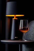 Glass of cognac or whiskey on dark table with modern lamp creating moody atmosphere. Luxury spirits photography with warm ambient lighting and selective focus.