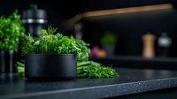 Fresh green herbs and dill in modern black bowl on dark kitchen counter with moody lighting, selective focus creates atmospheric culinary scene.