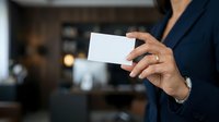 Businesswoman in navy blazer holding blank white business card in modern office environment for corporate branding and professional networking purposes.