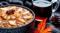 Warm bowl of apple cinnamon oatmeal with star anise garnish alongside coffee mug and autumn leaves on dark background, cozy breakfast setting.