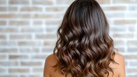 Woman with long wavy brown hair showing healthy shiny locks from behind against brick wall background for hair care and beauty salon concepts.