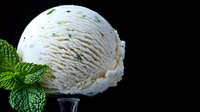 Creamy mint ice cream scoop garnished with fresh green mint leaves against dark background, showcasing refreshing dessert texture and natural flavors.