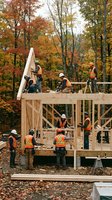 Construction crew in safety vests and hard hats building wooden house frame during autumn. Multiple workers installing walls and roof structure on residential construction site surrounded by fall foliage.