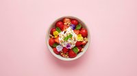 Fresh strawberry granola bowl with creamy yogurt and edible flowers on a soft pink background, top view. Healthy breakfast concept.