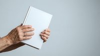 Mature man with brown skin holding blank white book or magazine against neutral background for publishing and marketing mockups.