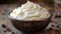 Creamy white whipped topping swirled in rustic brown ceramic bowl, scattered coffee beans on wooden surface create cozy atmosphere for food photography.