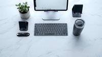Modern minimalist workspace with computer monitor, wireless keyboard, smartphone and coffee cup on white marble desk for productivity and remote work.