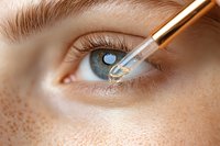 Close-up of eye drops application showing transparent liquid falling into blue eye with visible freckles and long eyelashes, demonstrating medical procedure.