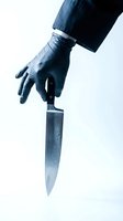 Hand in black latex glove holding sharp kitchen knife with water droplets on blade against white background for crime thriller concepts.