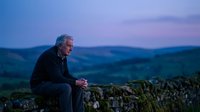 Senior Caucasian man sitting on stone wall during twilight hour in countryside. Contemplative elderly person enjoying peaceful evening outdoors.