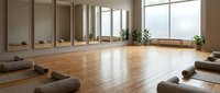 Spacious yoga studio with wooden floors, meditation cushions, and large windows creating peaceful atmosphere for wellness practice and mindfulness training.