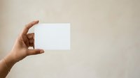 Hand holding blank white card against neutral beige background, suitable for business branding, marketing mockups, and promotional material presentations.
