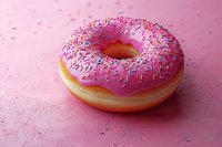 Pink frosted donut with colorful sprinkles on pink textured background, sweet dessert pastry with glazed topping for food and bakery designs.