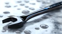 Chrome adjustable wrench on wet metallic surface with water droplets creating dramatic lighting effect and reflection, macro photography showing industrial detail.