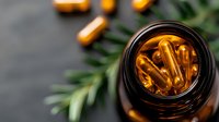 Amber glass bottle with omega-3 fish oil capsules and fresh rosemary sprigs on dark background, top view. Natural supplement for health and wellness.