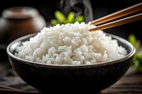 Steaming hot white rice in black ceramic bowl with wooden chopsticks on dark wooden table, Asian cuisine background.