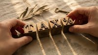 Hands arranging wooden letter blocks spelling tax word on striped fabric surface with natural lighting, suitable for accounting, finance, business, and tax-related publications.