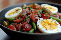 Fresh garden salad with halved boiled eggs, cherry tomatoes, green beans, and herbs in black bowl, dressed with olive oil and seasoned with pepper.