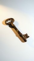 Ornate vintage bronze key with decorative handle casting shadow on white background for antique collection and security concepts.