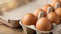 Fresh brown chicken eggs in cardboard carton on rustic wooden table surface for cooking and baking ingredients in kitchen food preparation.