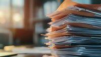 Stack of business documents and paperwork files on office desk with soft morning light, representing workload and administrative tasks in workplace.