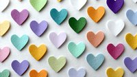 Colorful paper hearts scattered on white background creating romantic pattern for Valentine's Day crafts, wedding decorations and love-themed designs.